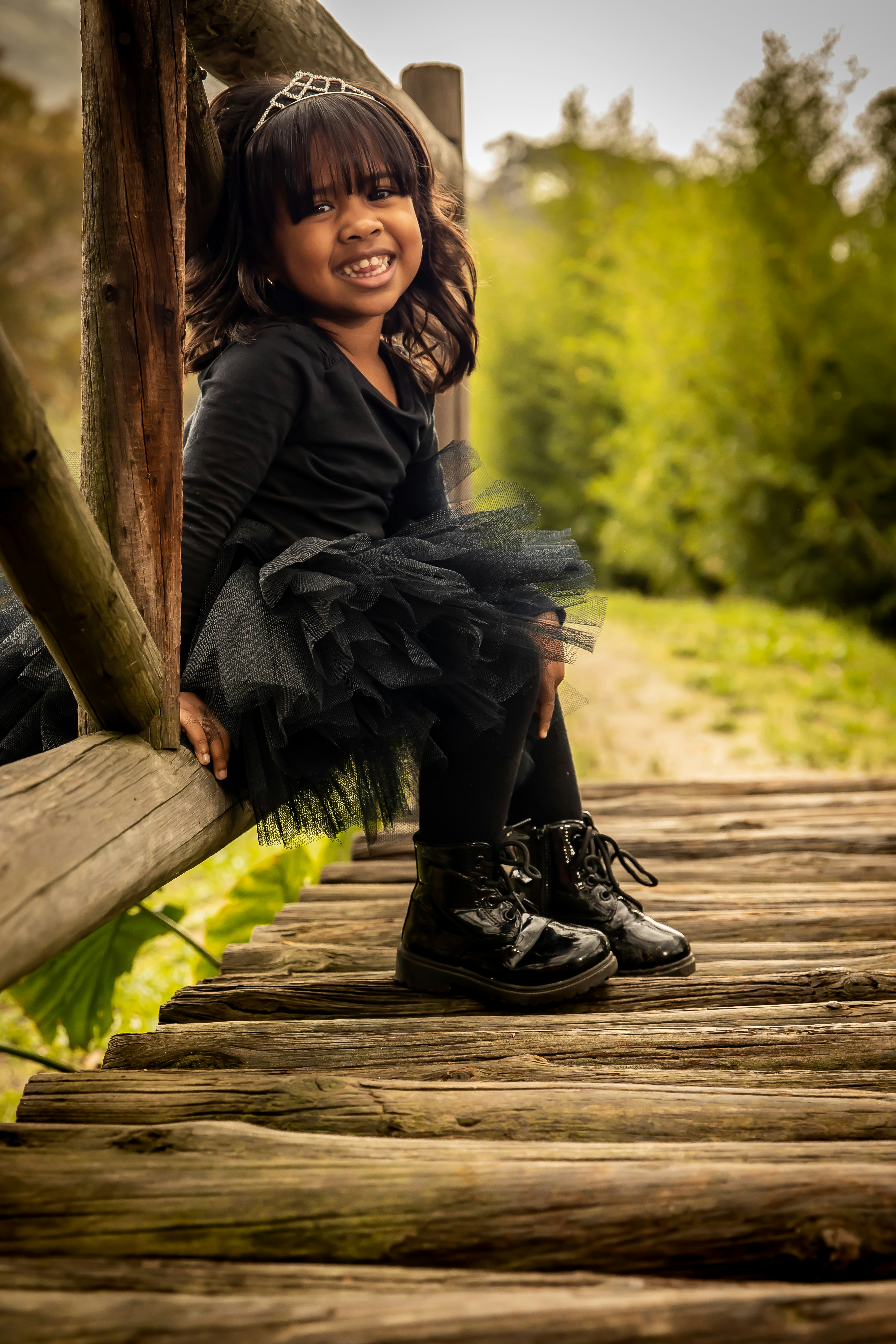 woman in black long sleeve dress sitting on brown wooden bridge